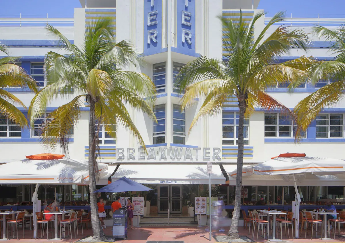 Front facade of Hotel Breakwater South Beach with Art Deco design, palm trees, and outdoor dining on Ocean Drive.