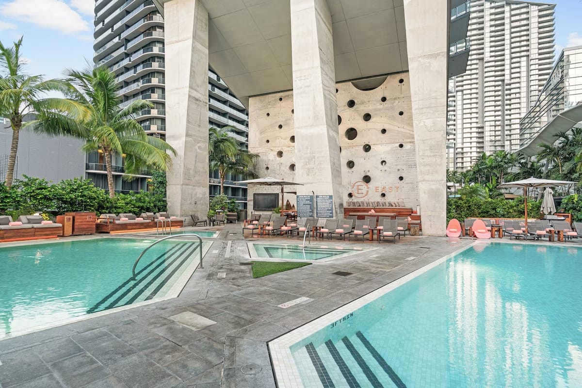 Multiple outdoor pools at EAST Miami in Brickell with skyline views, lounge seating, palm trees, and modern urban resort design.