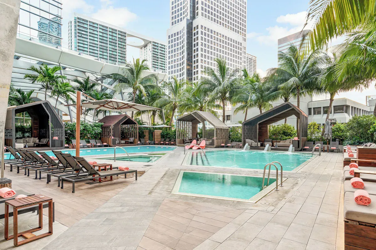 Resort-style outdoor pool deck at EAST Miami in Brickell with palm trees, private cabanas, lounge chairs, and multiple pools in a luxury urban setting.