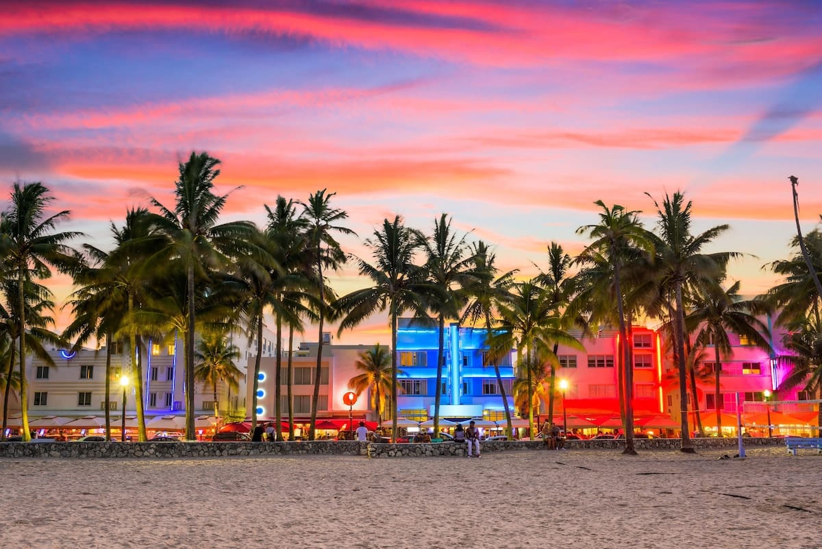 Ocean Drive in South Beach at sunset with neon hotels and palm trees — walkable nightlife and dining near The Betsy Hotel.