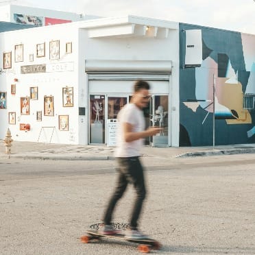 A skateboarder glides through the vibrant streets of Wynwood, surrounded by colorful murals and urban art.